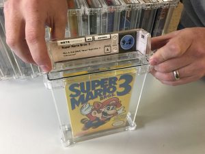 Two hands seal a boxed NES game into a clear container.