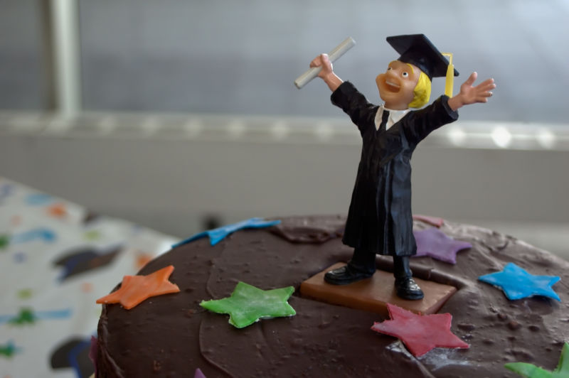 A chocolate cake is decorated by the plastic figurine of a celebratory graduate, complete with diploma and mortarboard.