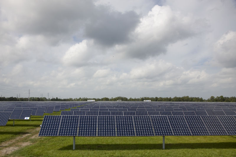 Rows of solar panels under a cloudy sky.