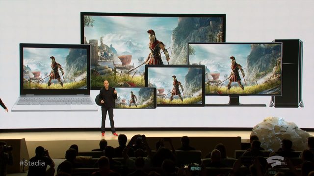 A man gives a presentation to a crowded theater in front of a large screen.