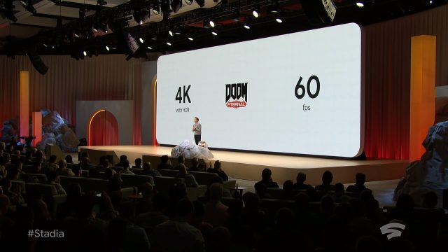 A man gives a presentation to a crowded theater in front of a large screen.