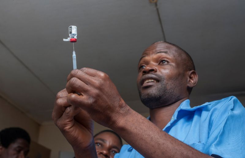 A man stabs a needle into a jar of liquid.