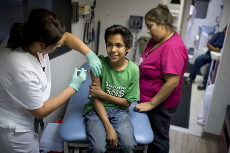 A boy smiles as he gets a measles, mumps, and rubella (MMR) vaccination.