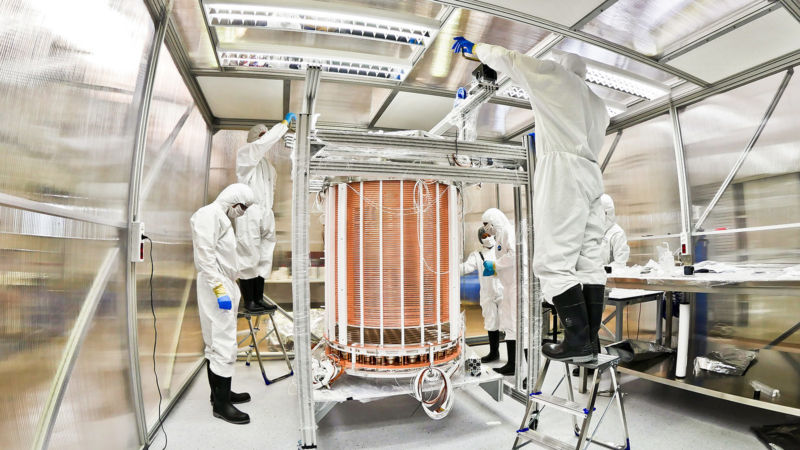 People in clean suits stand around a detector at the waist of a person.