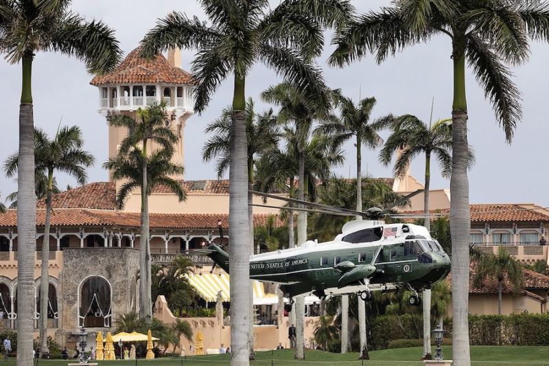 Large helicopter emblazoned with presidential logos lands at a seaside resort.