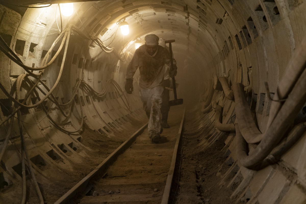 Two men walk through a dusty tunnel.