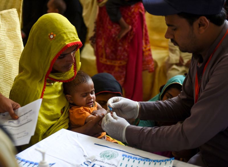 A man takes a blood sample from a child sitting in its mother's lap.