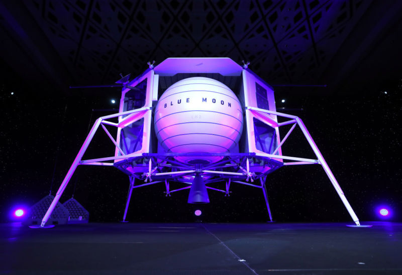 A man on a stage stands in front of the life-size model of a spaceship.