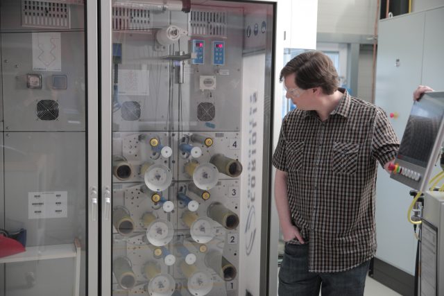 Ars' Lee Hutchinson stands in front of the creel cabinet that feeds carbon fibre to the robot that took all of our carbon fibre layup jobs.