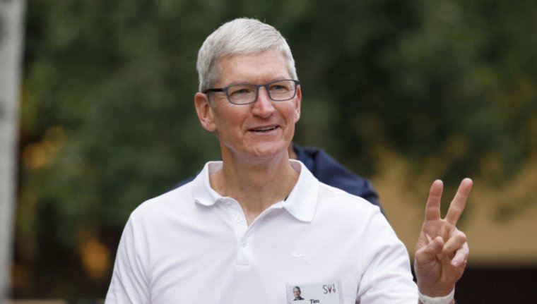 An older man in a white polo shirt flashes a peace sign while walking outdoors.