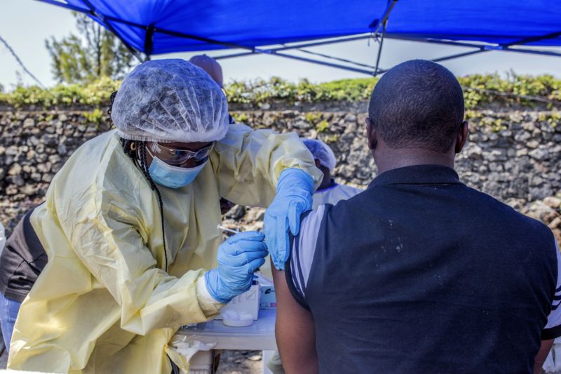 A nurse in PPE administers a shot to a man in an outdoor clinic.