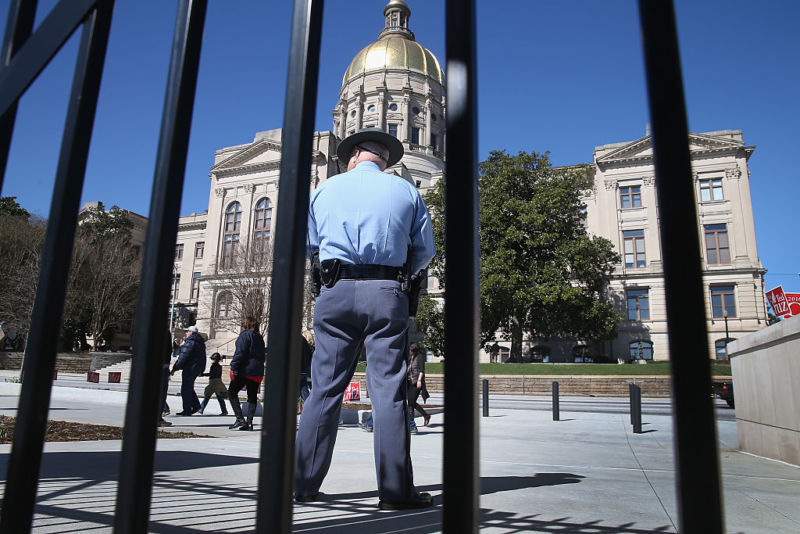A uniformed police officer stands outside a courthouse with a rotunda.