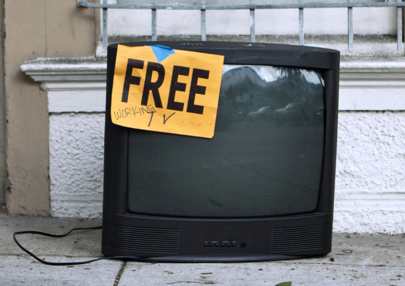 A television left on a sidewalk with a sign saying: 