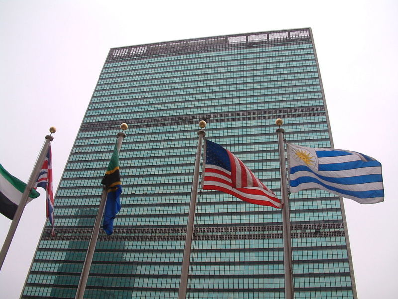 Glass and steel skyscraper with flags of multiple nations in front of it.