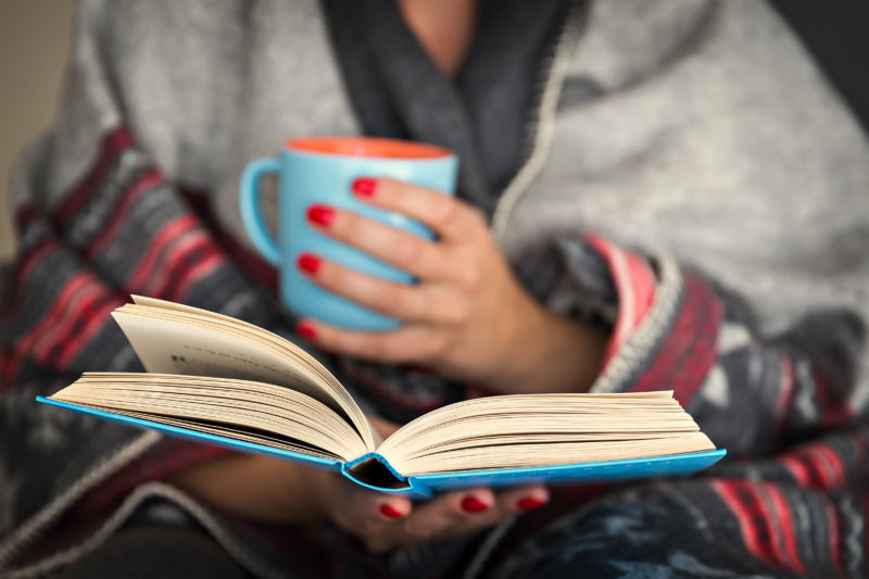 Stock photo of a woman wrapped in a blanket reading a book.