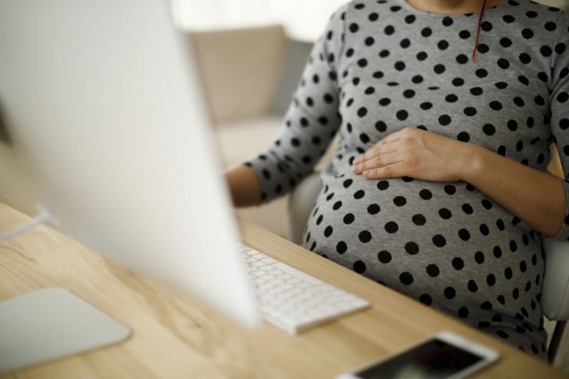 A pregnant woman operates a computer.