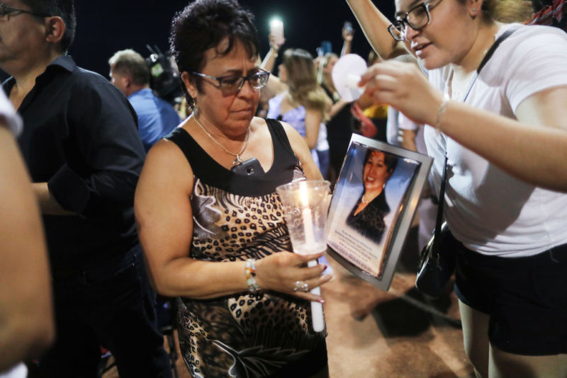 At an interfaith vigil for victims of a mass shooting in El Paso, Texas, a woman carries a candle and a photo of Elsa Mendoza Marquez, who died in the shooting.