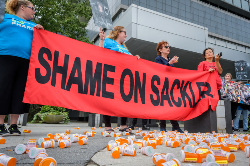 Protestors hold up a banner while surrounded by empty prescription bottles.