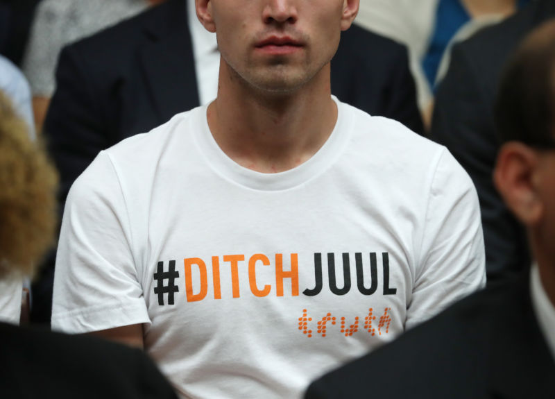 A young man wears a shirt that reads DITCHJUUL while James Monsees, co-founder and chief product officer at JUUL Labs Inc., testifies before the House Economic and Consumer Policy Subcommittee, which is examining JUUL's role in the youth nicotine epidemic, on July 25, 2019, in Washington, DC.
