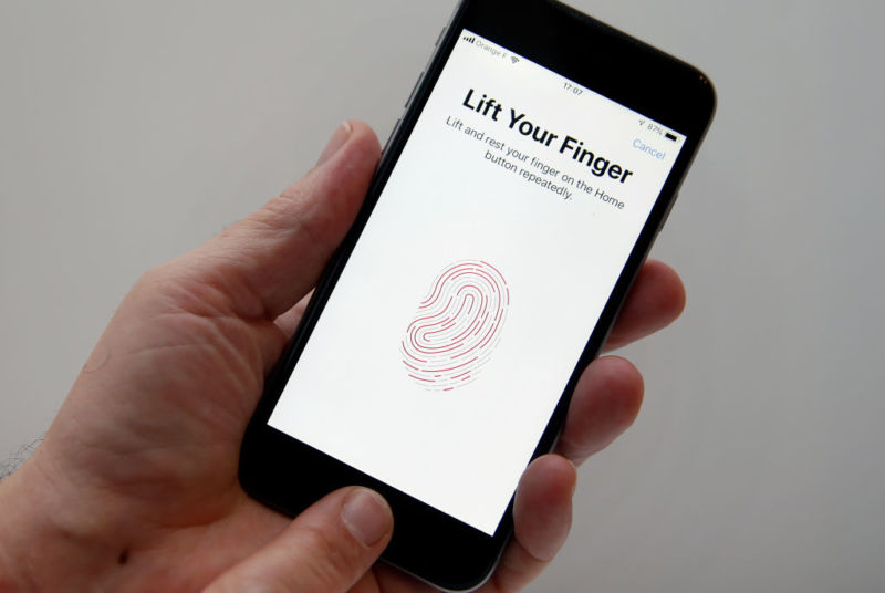 A person's hand holding an iPhone while setting up the Touch ID fingerprint reader feature.