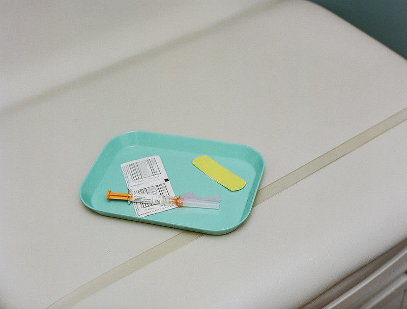 A hypodermic needle sits on a tray next to a bandage and an alcohol wipe.