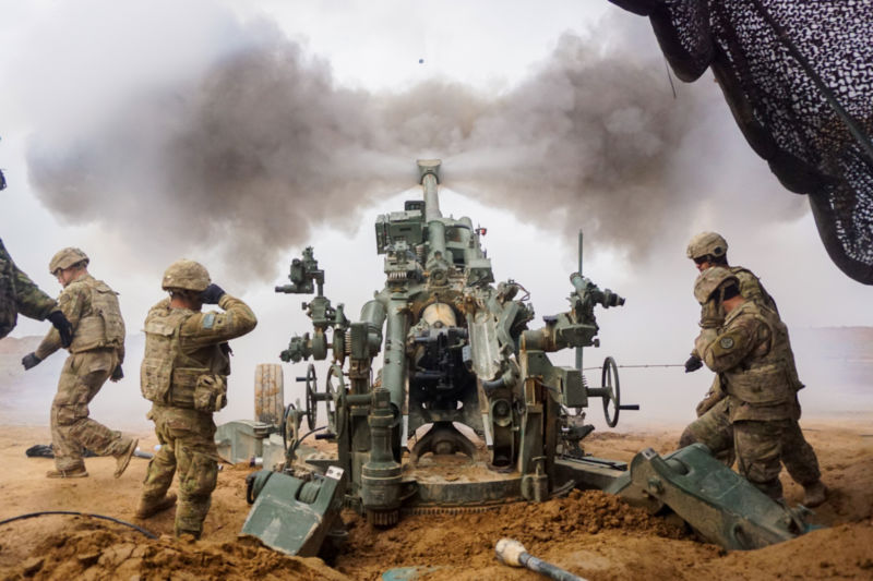 Soldiers in combat gear fire a gigantic gun.