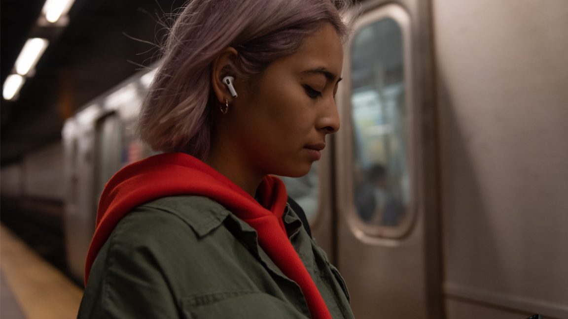 Promotional image of hip woman using Airpods on subway.