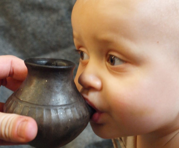 Photo of a baby drinking from a replica clay vessel.