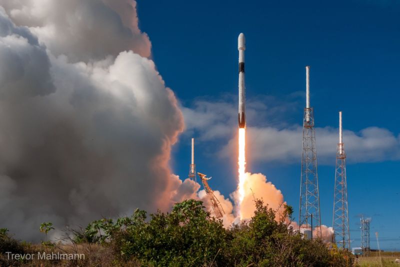 Smoke and flame follows a rocket as it lifts into blue sky.