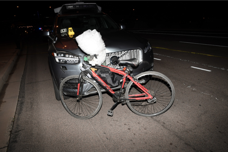 A bicycle leans against the front of an SUV at night.