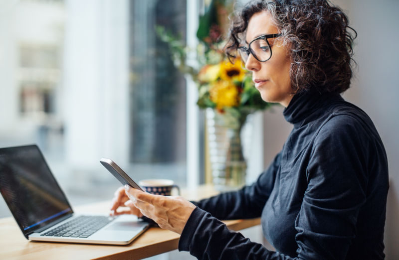 Stock photo of a woman using a smartphone and a notebook computer in a cafe.