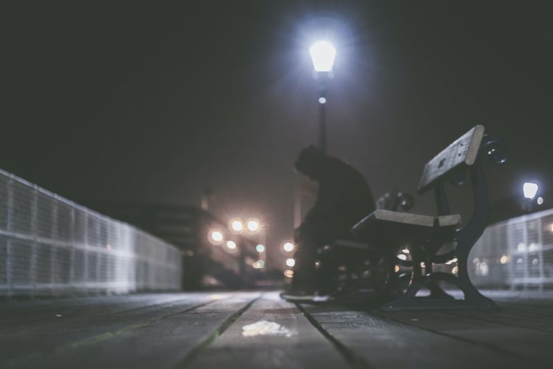 A lonely person sitting on a bench at night.