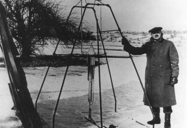 Robert H. Goddard, bundled against the cold weather of March 16, 1926, holds the launching frame of his most notable invention — the first liquid-fueled rocket, an example of a 