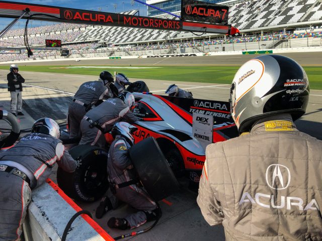 Crewmembers swarm over a prototype race car during a pitstop