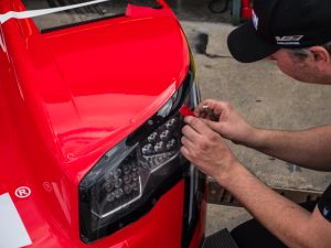 A mechanic applies tape to the headlights of a racing car.