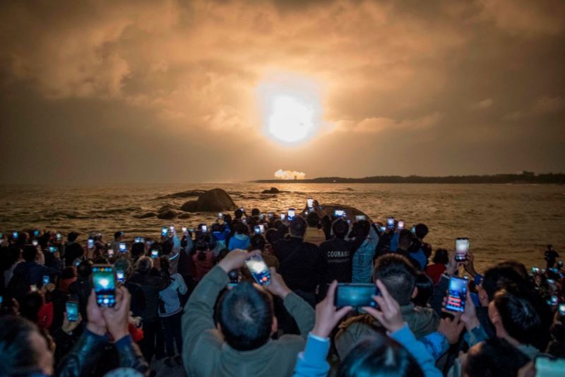 People take photos as China's heavy-lift Long March 5 rocket fires from its launch center in Wenchang, southern China's Hainan province, on December 27, 2019.