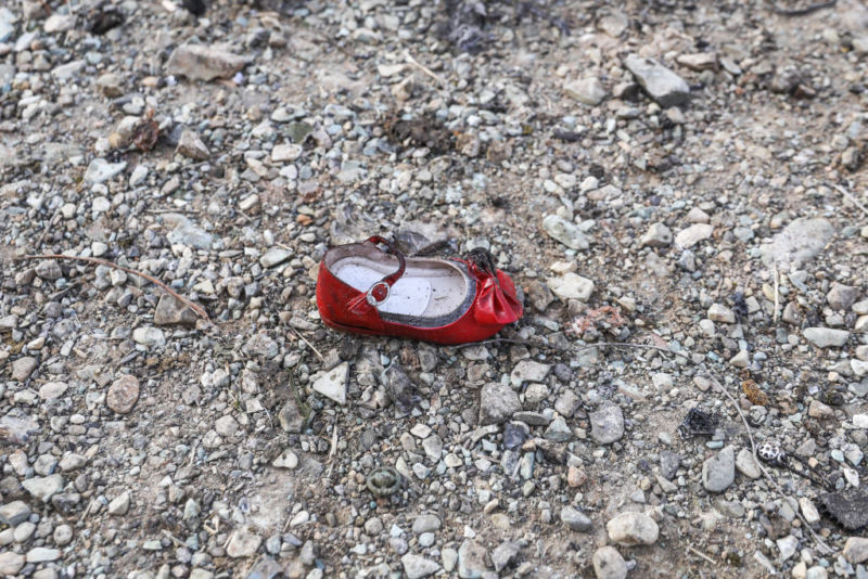 A battered red shoe with a bow on it sits in a rugged field.