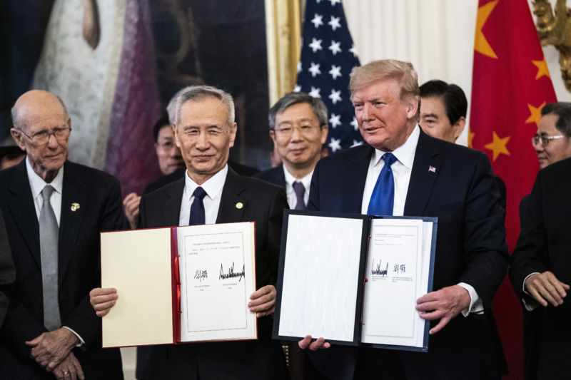 Two men in suits hold up signed documents.