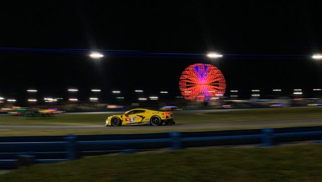 A yellow race car at night, with a red Ferris wheel in the background.
