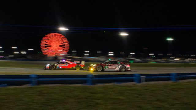 An Acura prototype race car passes a plaid porsche at night