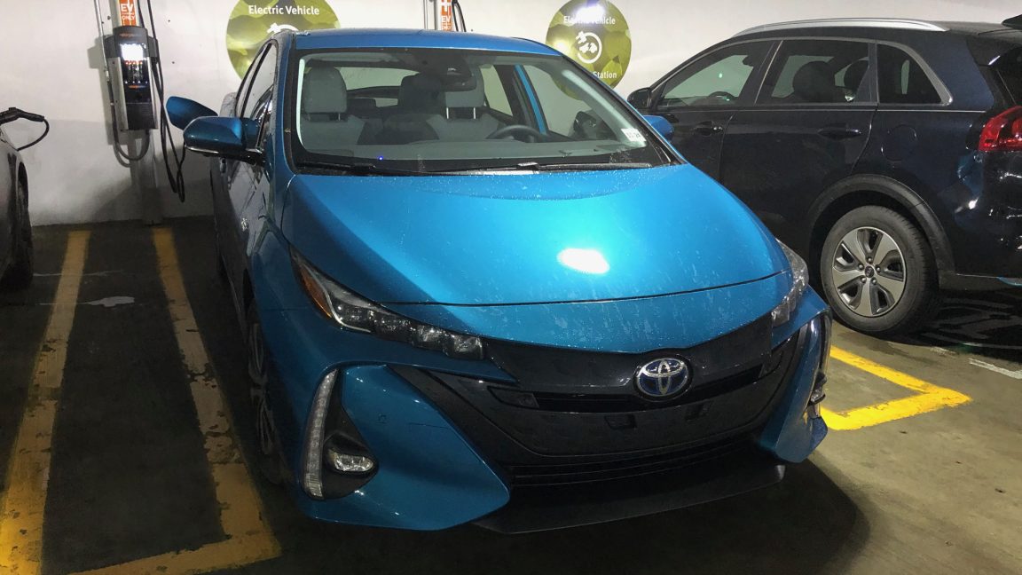 A blue Toyota Prius Prime plugged into an electric car charger