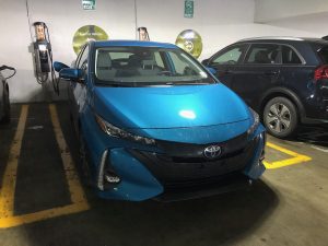 A blue Toyota Prius Prime plugged into an electric car charger