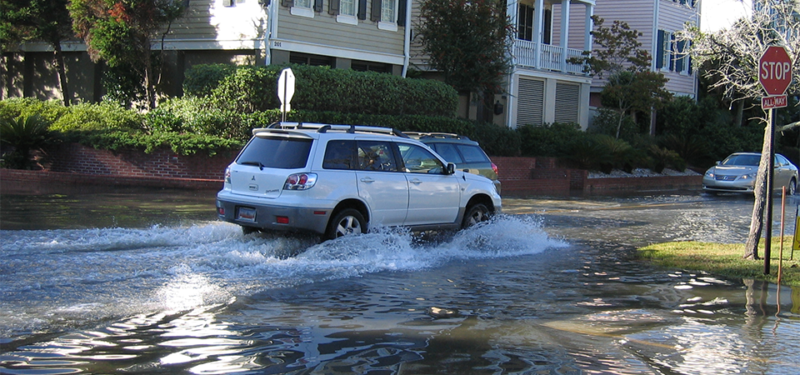 Image of a car driving through a flooded street.