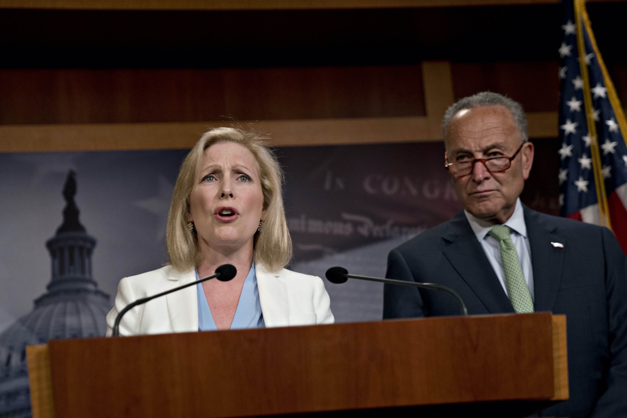 Senator Kirsten Gillibrand speaks at a podium during a news conference while Senate Minority Leader Chuck Schumer looks on.