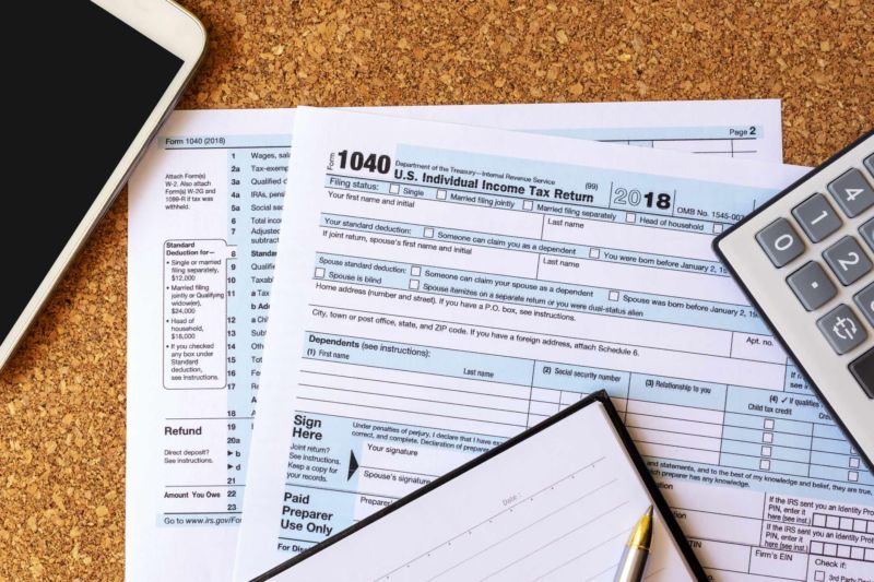 A US individual income tax return document lying on a table next to a calculator, notebook, pen, and iPad.