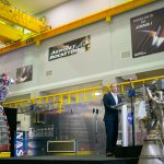 A man speaks from a podium in a space vehicle factory.