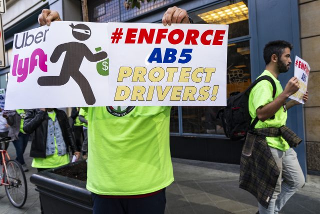 In light of AB 5, Uber and Lyft drivers hold placards during a protest against the ridesharing companies' low wages in Los Angeles, California. 