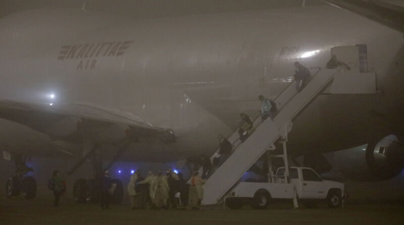 Passengers use mobile stairs to exit and jet plane at night.