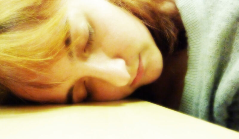 Closeup photo of a woman sleeping with her head on a desk.