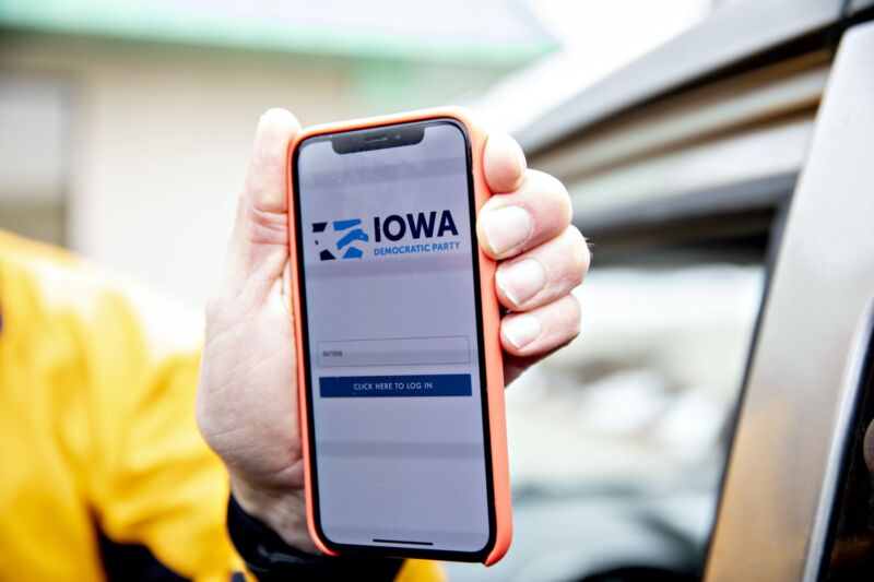 A man's hand holding an iPhone displaying the Iowa Democratic Party's app for reporting caucus results.